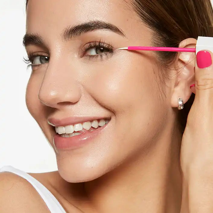 Smiling woman applying fLASH eyelash serum with applicator for longer lashes