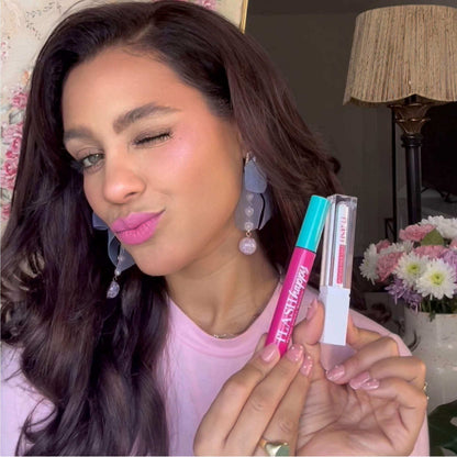 Woman with long lashes holding eyelash serum duo, wearing pink makeup, floral background